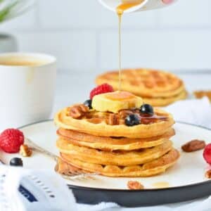 Coconut Flour Waffles stacked on a plate with maple syrup poured on top