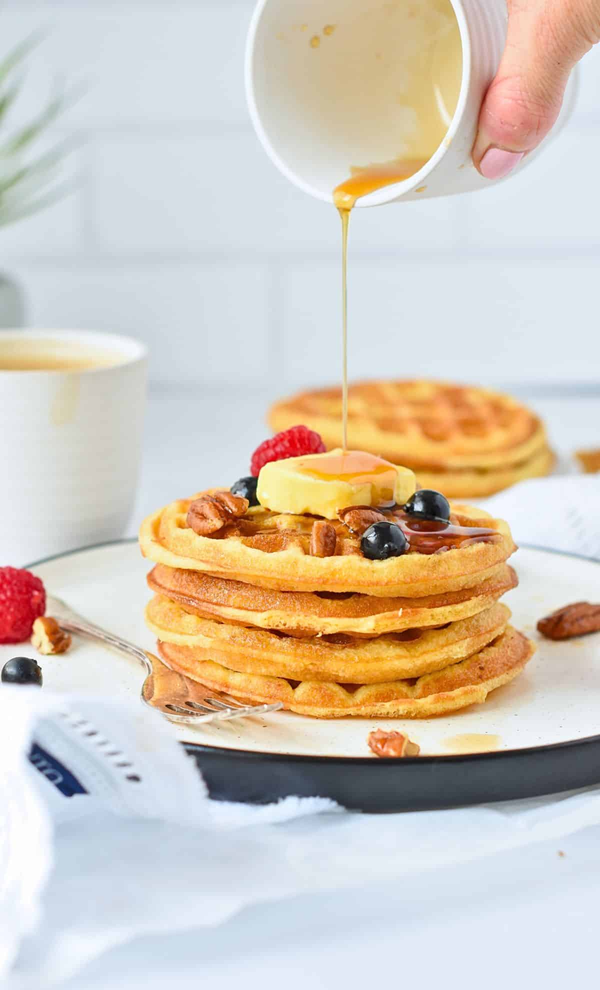 Coconut Flour Waffles stacked on a plate with maple syrup poured on top