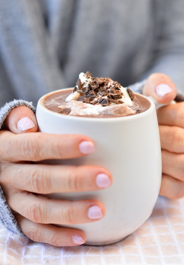Holding a cup of keto hot chocolate decorated with whipped coconut cream and chocolate chips.
