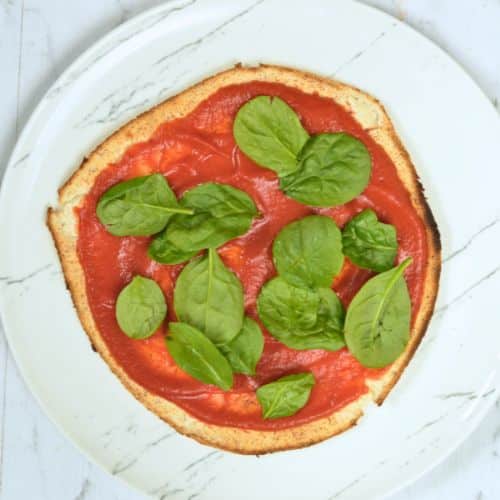 Prebaked Coconut Flour Pizza Crust with tomato sauce and basil.