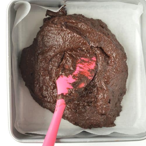 Date Brownies batter in a square pan lined with parchment paper.