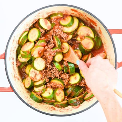 Stirring Zucchini Pizza Casserole in a cast-iron pan.