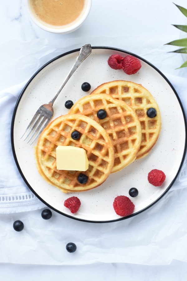 Three keto waffles with coconut flour on a large plate with butter, raspberries, and blueberries.
